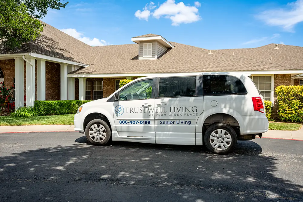 Plum Creek Place-POI-01 A white van labeled "Trustwell Living Senior Living" is parked outside a residential building on a sunny day.