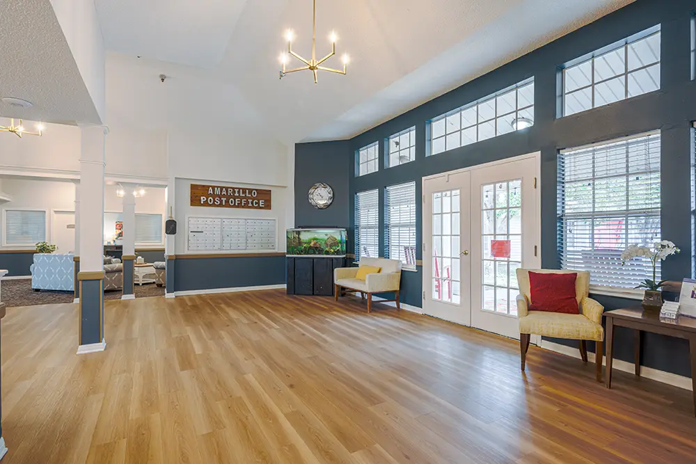 Plum Creek Place-POI-07 Spacious room with wood flooring, large windows, a "Post Office" wall display, yellow chair, aquarium, and decorative items on tables.