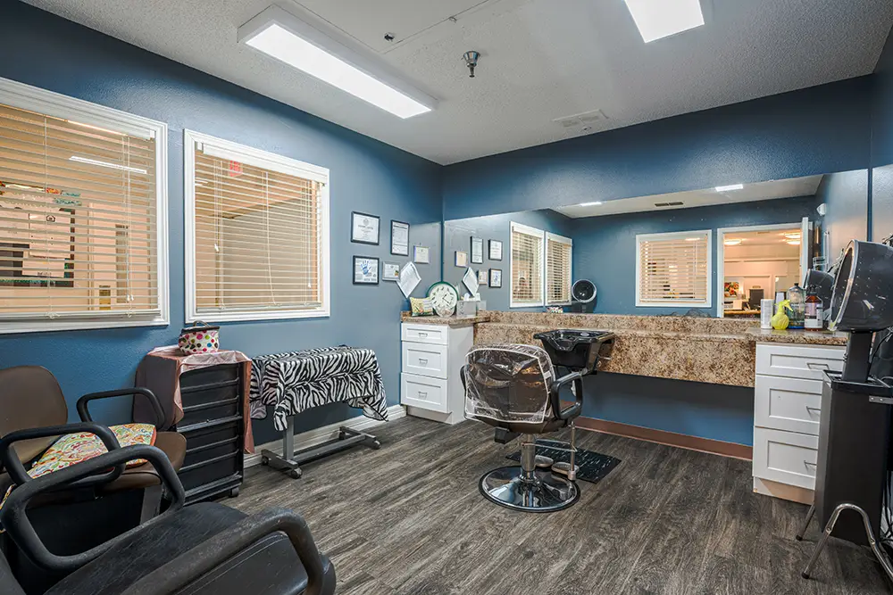 Plum Creek Place-POI-15 Modern hair salon with blue walls, a large mirror, two salon chairs, a zebra-striped towel, storage drawers, and framed pictures on the wall. Bright overhead lighting.
