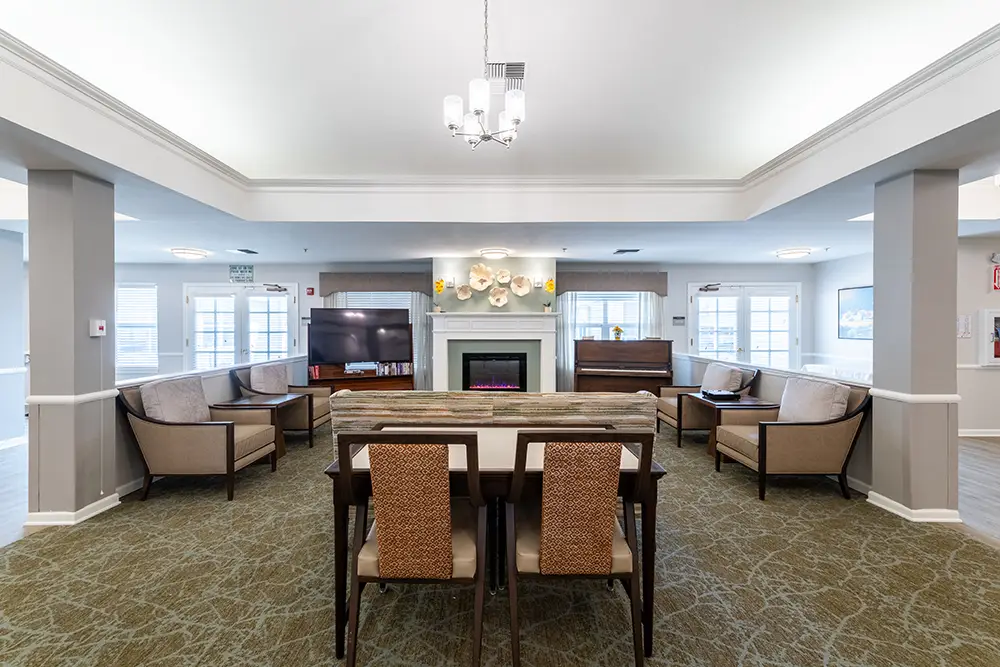 Spacious lounge with a central table, chairs, sofas, a fireplace, TV, and large windows letting in natural light. Spacious lounge with a central table, chairs, sofas, a fireplace, TV, and large windows letting in natural light.