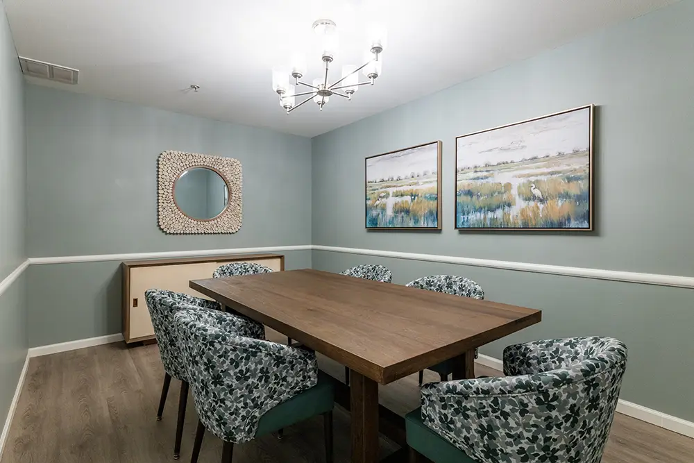 Dining room with a wooden table, six patterned chairs, two landscape paintings, a round mirror, chandelier, blue-green walls, and wood flooring. Dining room with a wooden table, six patterned chairs, two landscape paintings, a round mirror, chandelier, blue-green walls, and wood flooring.