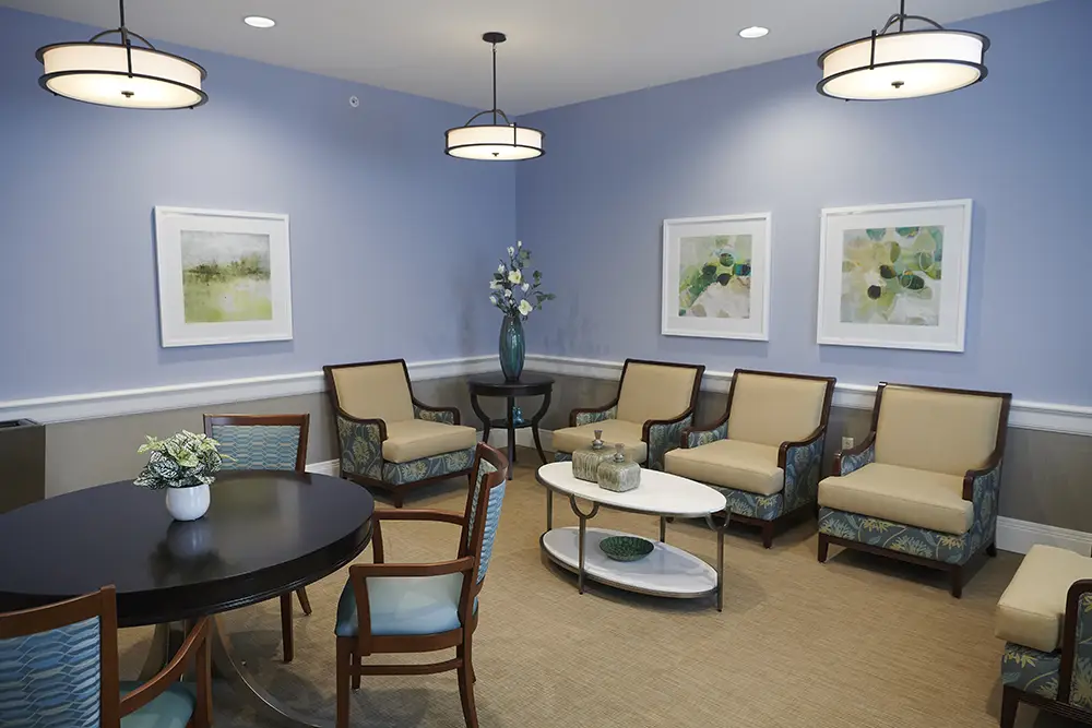 TWRH14 A waiting room with light blue walls, modern armchairs, a round table with chairs, three wall art pieces, and a vase with flowers on a side table.
