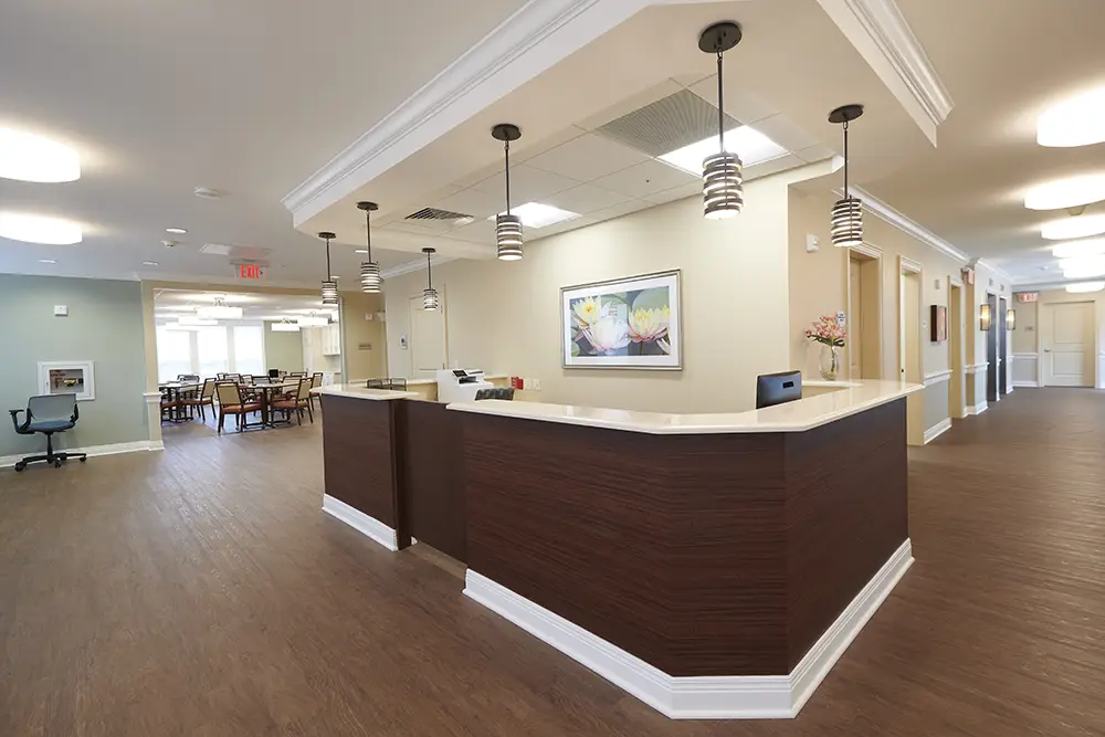 TWRH18 Reception area in a modern, well-lit office or healthcare facility with wood floors, a central desk, pendant lights, and a seating area in the background.