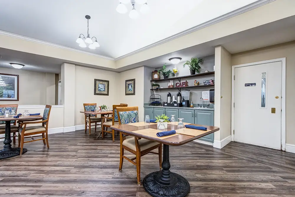 Small dining area with wooden tables and chairs, place settings, a beverage station, and wall decor. The floor is wood and there’s a door labeled “restroom” on the right. Small dining area with wooden tables and chairs, place settings, a beverage station, and wall decor. The floor is wood and there's a door labeled "restroom" on the right.