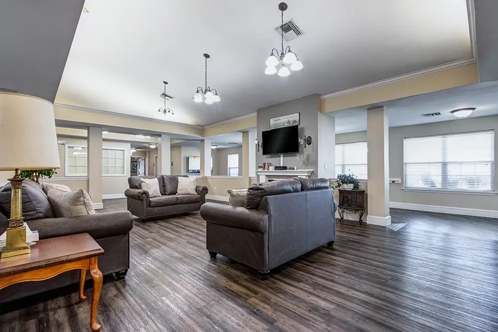 Spacious living room with brown sofas, a wall-mounted TV, wood flooring, light walls, and large windows letting in natural light. Spacious living room with brown sofas, a wall-mounted TV, wood flooring, light walls, and large windows letting in natural light.