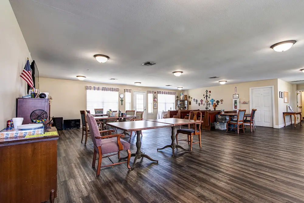 Spacious community room with wooden floor, tables, and chairs. Walls have decorations, flags, and lights. Large windows let in natural light. Spacious community room with wooden floor, tables, and chairs. Walls have decorations, flags, and lights. Large windows let in natural light.