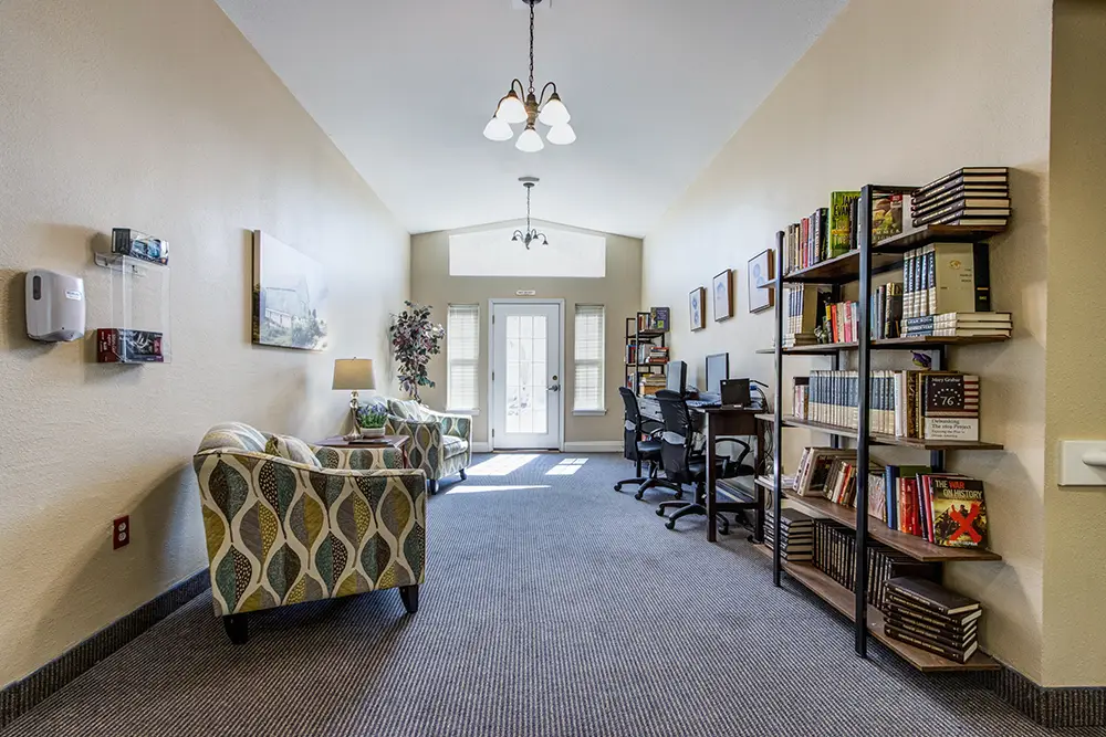 A well-lit room with armchairs, bookshelves, computers on desks, and a glass door at the far end, decorated with plants and artwork. A well-lit room with armchairs, bookshelves, computers on desks, and a glass door at the far end, decorated with plants and artwork.