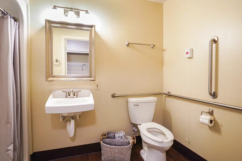 Accessible bathroom with grab bars, a wall-mounted sink, toilet, towel rack, toilet paper holder, and a basket with towels on the floor. Accessible bathroom with grab bars, a wall-mounted sink, toilet, towel rack, toilet paper holder, and a basket with towels on the floor.