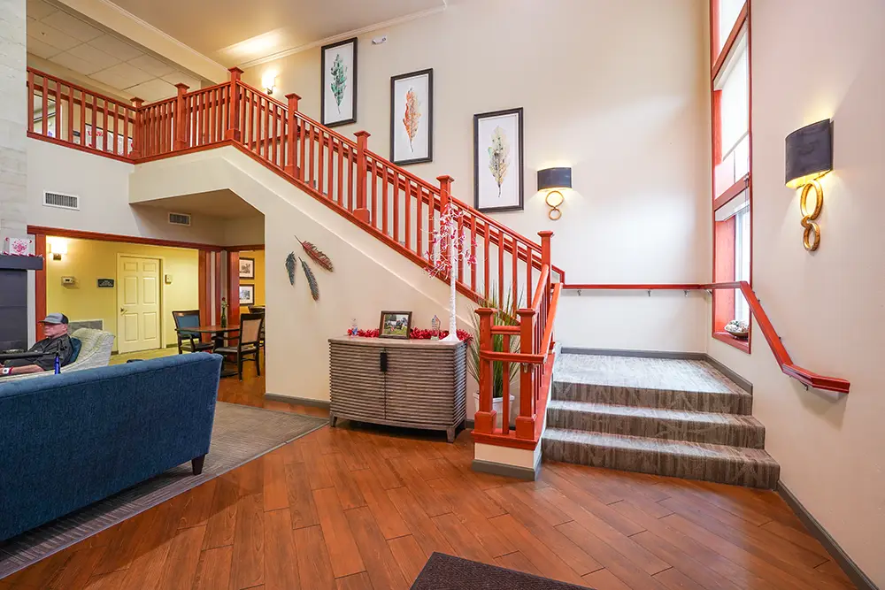 A lobby with wooden floors, blue seating, red staircase, framed art on walls, and a console table decorated with vases and plants. A lobby with wooden floors, blue seating, red staircase, framed art on walls, and a console table decorated with vases and plants.
