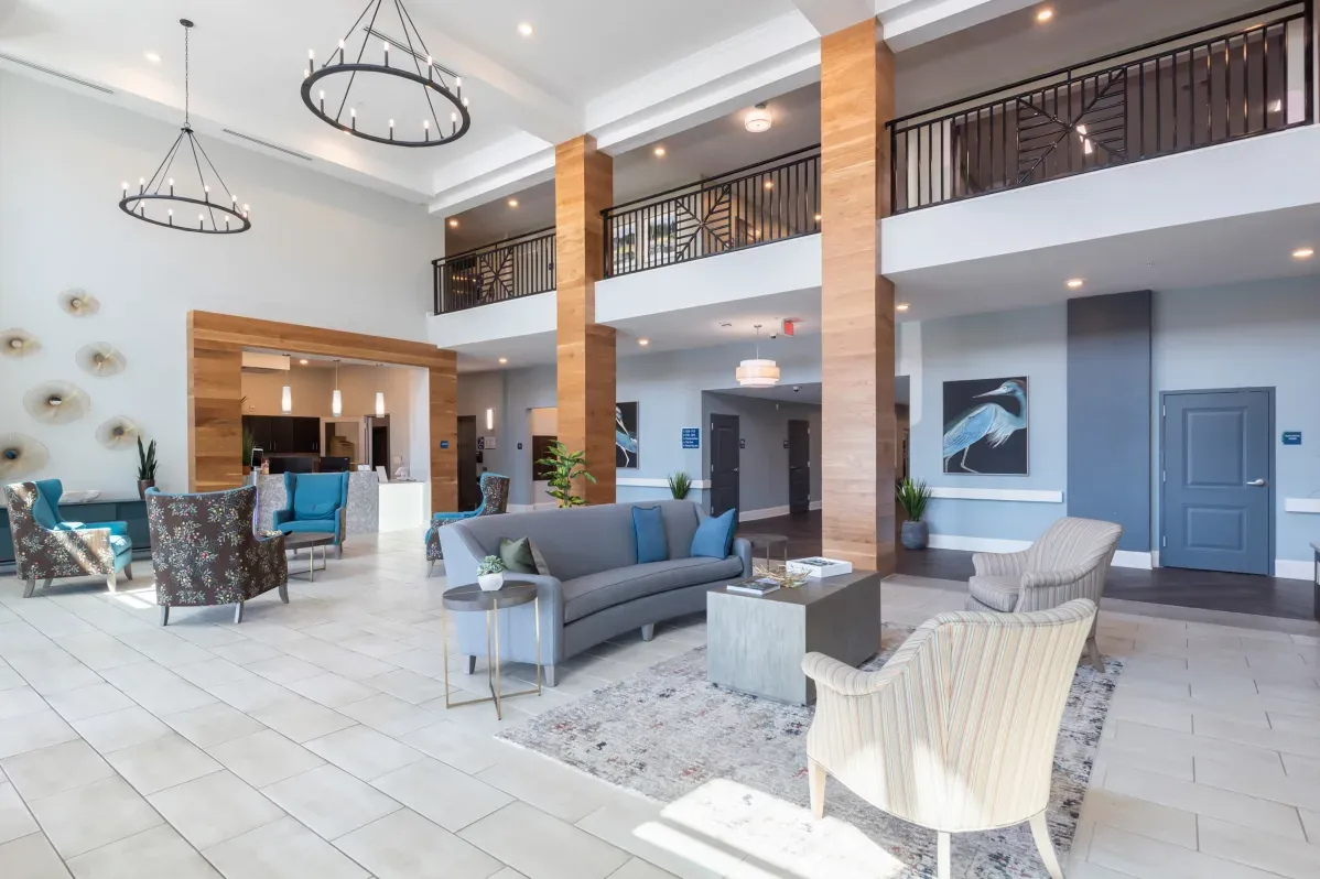 Modern hotel lobby with high ceilings, large windows, seating areas, decorative wall art, and wood accents—designed with the welcoming comfort found in Trustwell Senior Living communities.