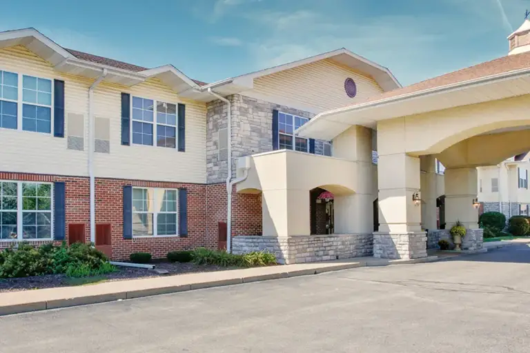 Two-story Trustwell Senior Living building with a mix of brick and siding exterior, large windows, stone accents, and a covered entrance driveway.